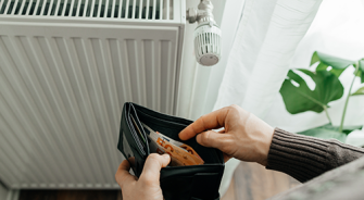 The man's hands hold a wallet with money next to the radiators. The concept of increasing prices for gas and energy. Energy crisis in Europe.